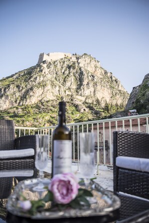 A table with a bottle and glasses, overlooking a mountainous landscape with a castle. - Asimoni Pension (Nafplio)