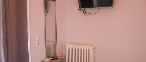 A hotel room with a bed, a small desk, a chair, a television, a mirror, and a radiator.