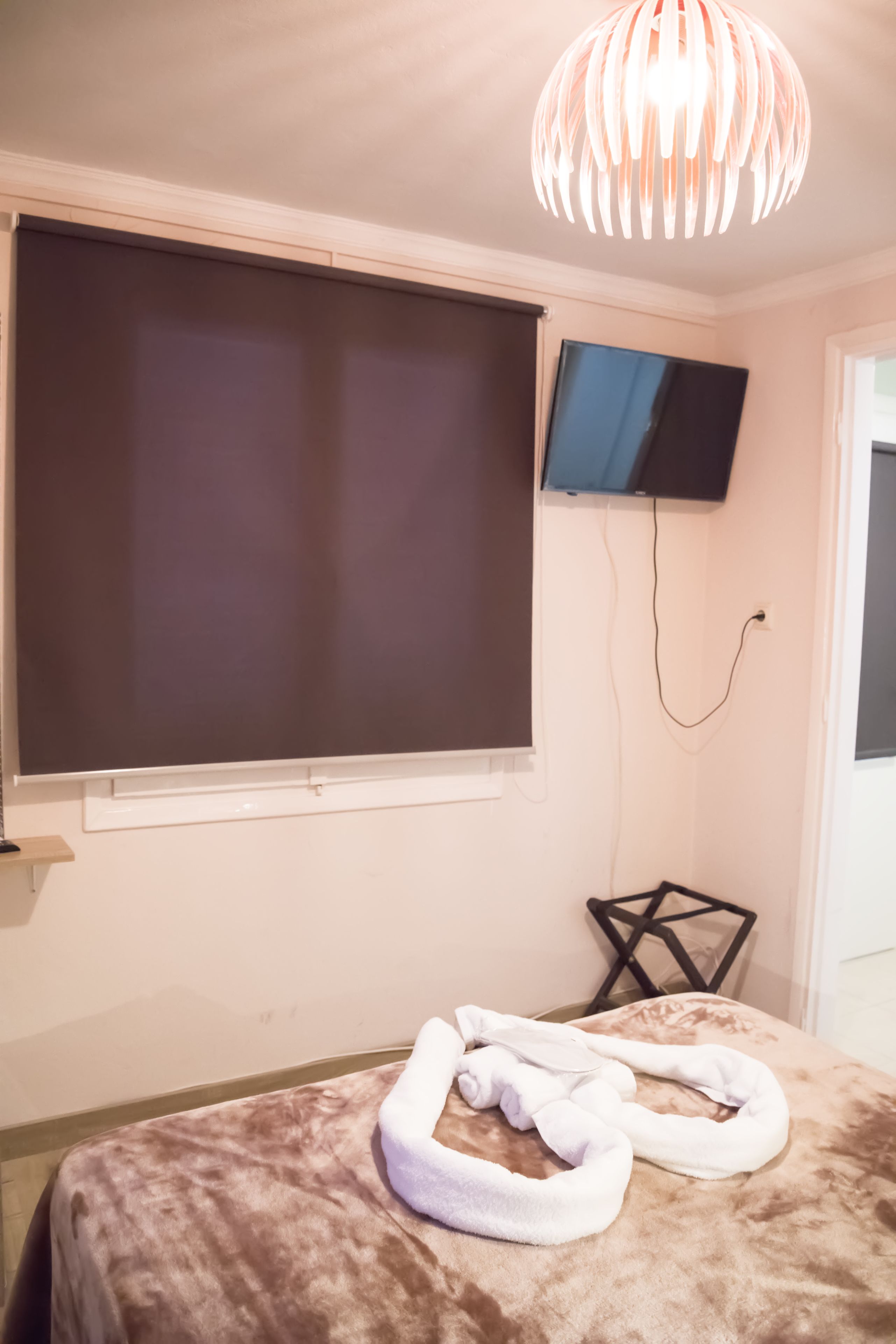 A room with a large bed, a flat-screen TV mounted on the wall, and a unique ceiling light fixture.