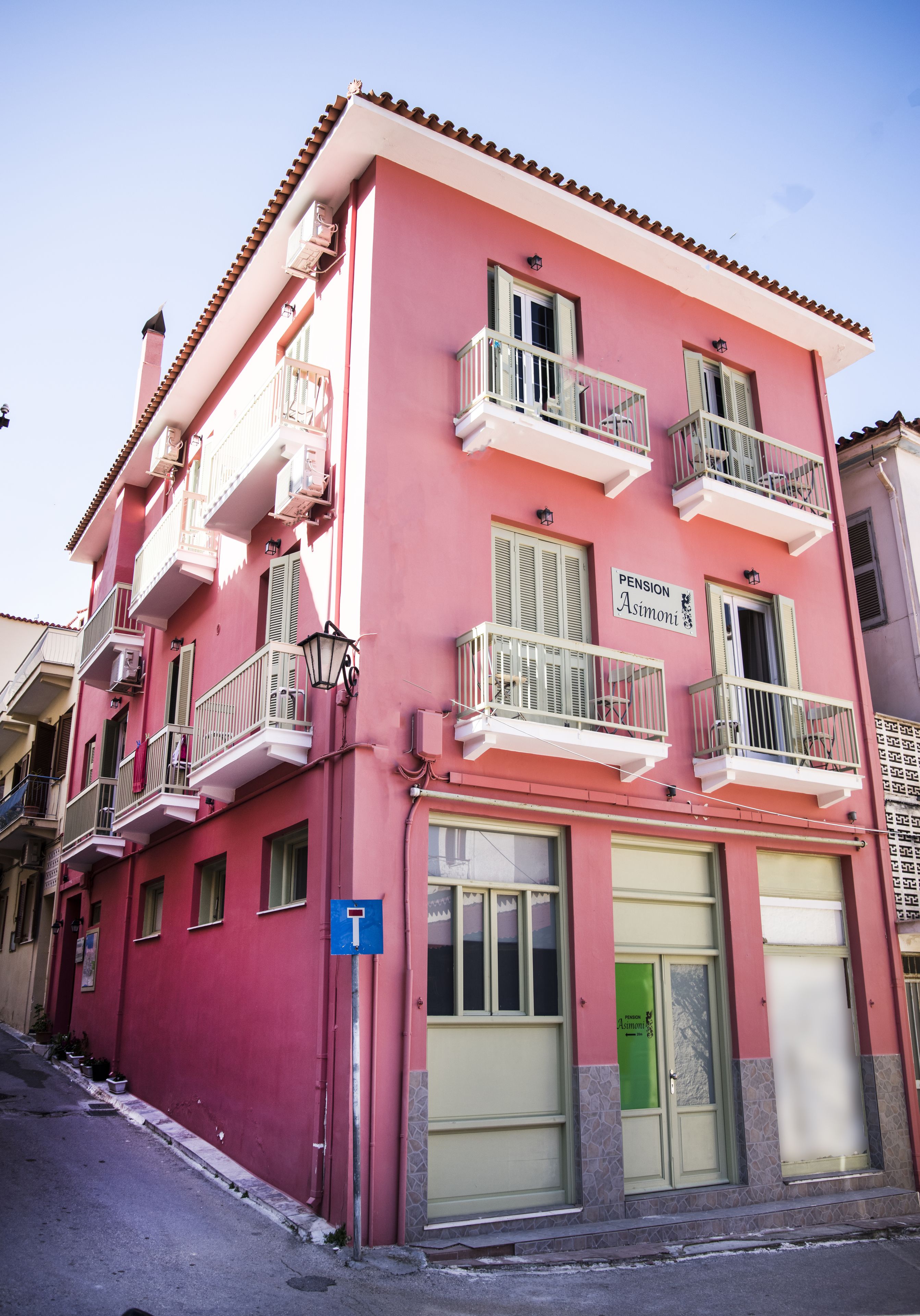A pink building with balconies, a green door, and a sign reading "Pension Asimini".