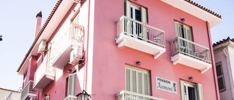 A pink building with balconies, a green door, and a sign reading "Pension Asimini".