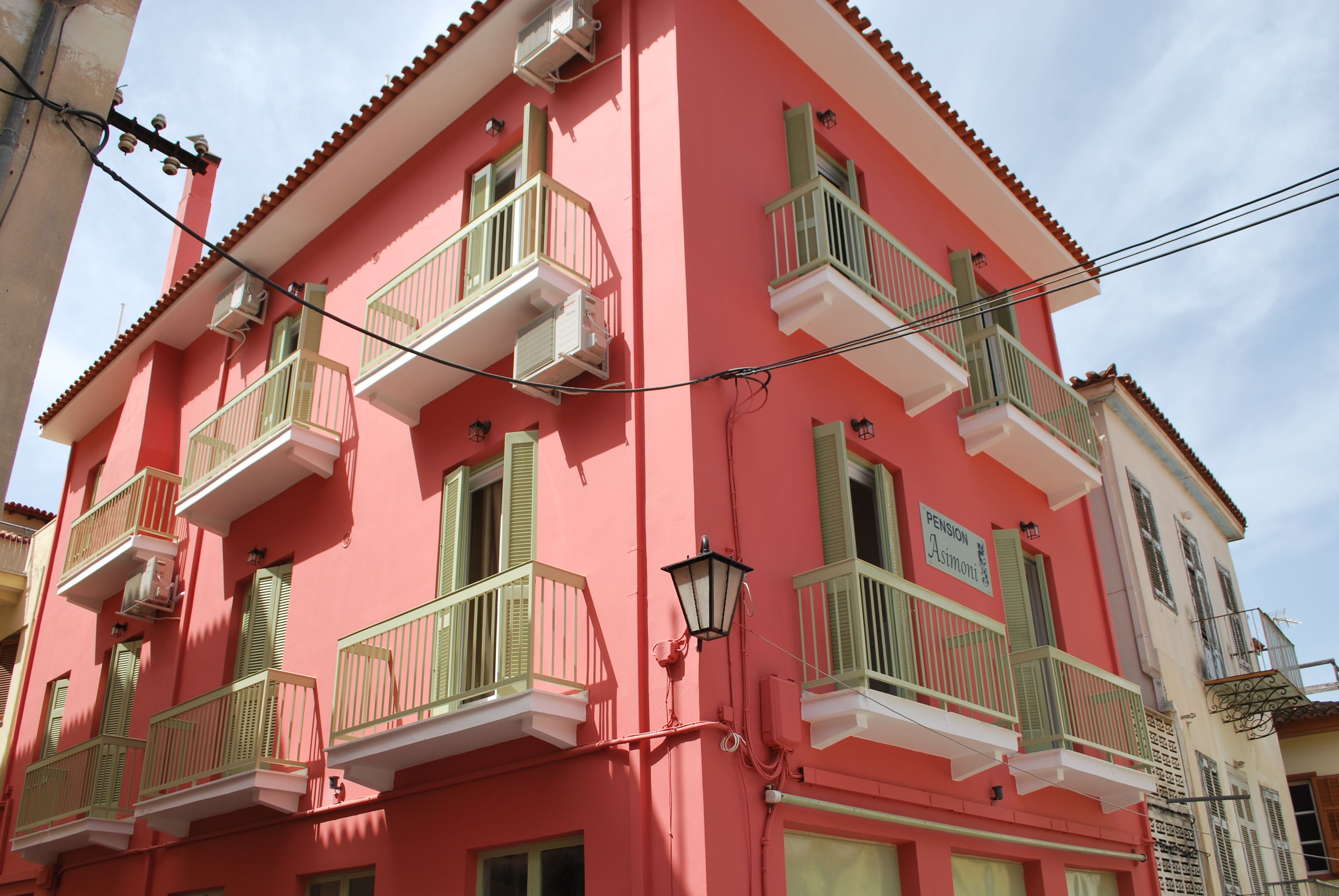 A pink building with green balconies and a sign that reads "Pension Asimonti".