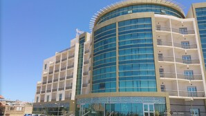 A modern hotel with a curved glass facade, multiple balconies, and a prominent flag. - Al Mansour Palace (Mazagran)