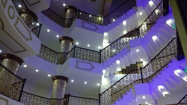 A multi-level interior with a central staircase, patterned railings, and multiple light fixtures. - Al Mansour Palace (Mazagran)