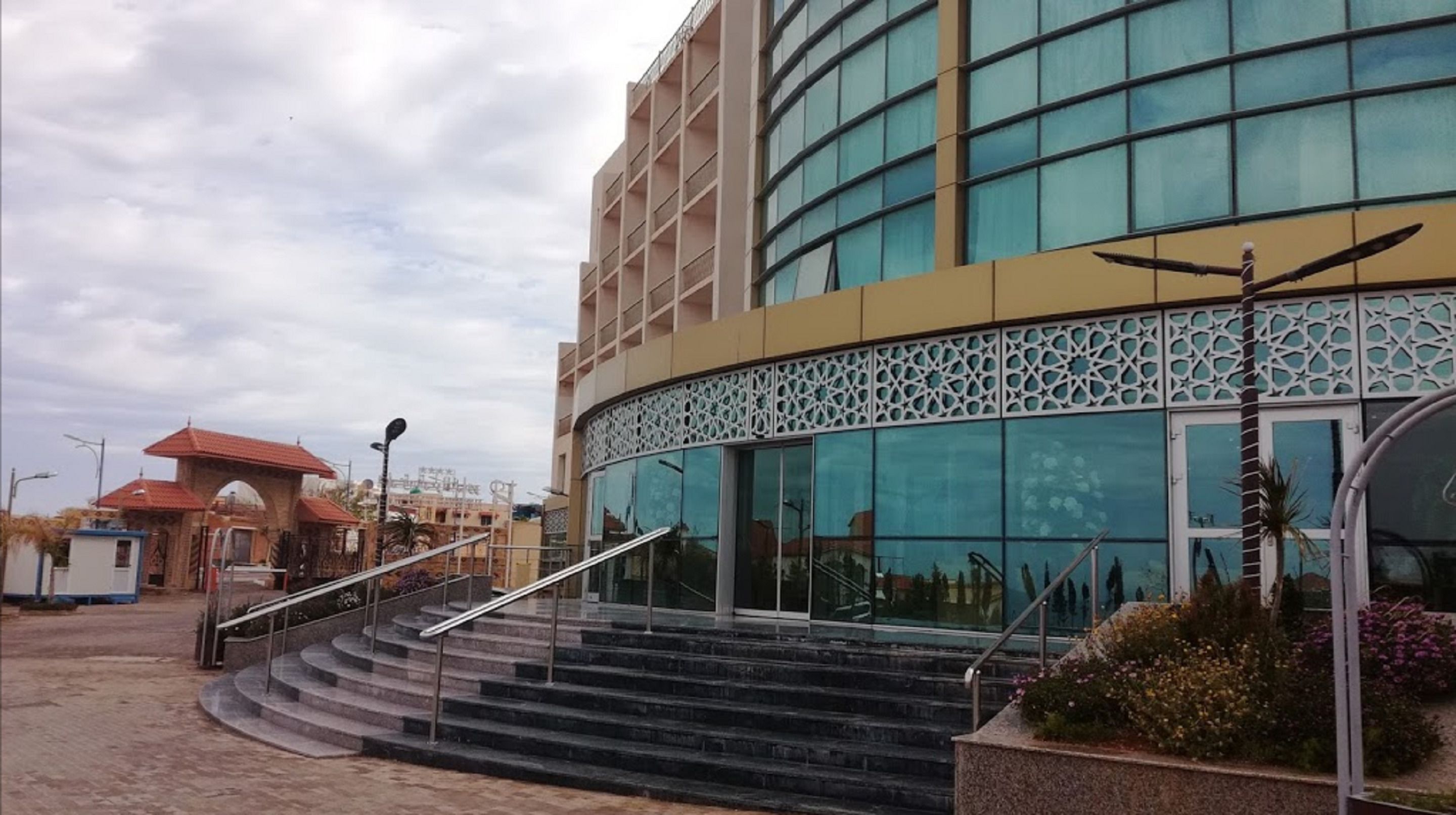 A modern building with a curved glass facade, a set of outdoor stairs leading to the entrance, and a decorative metal fence.