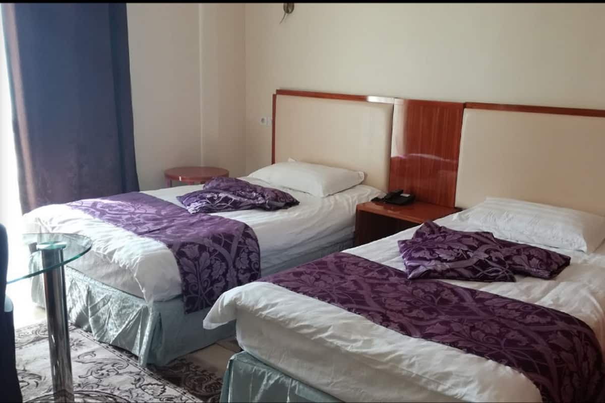 Twee eenpersoonsbedden met hoofdborden, nachtkastjes en een glazen tafel met stoel.