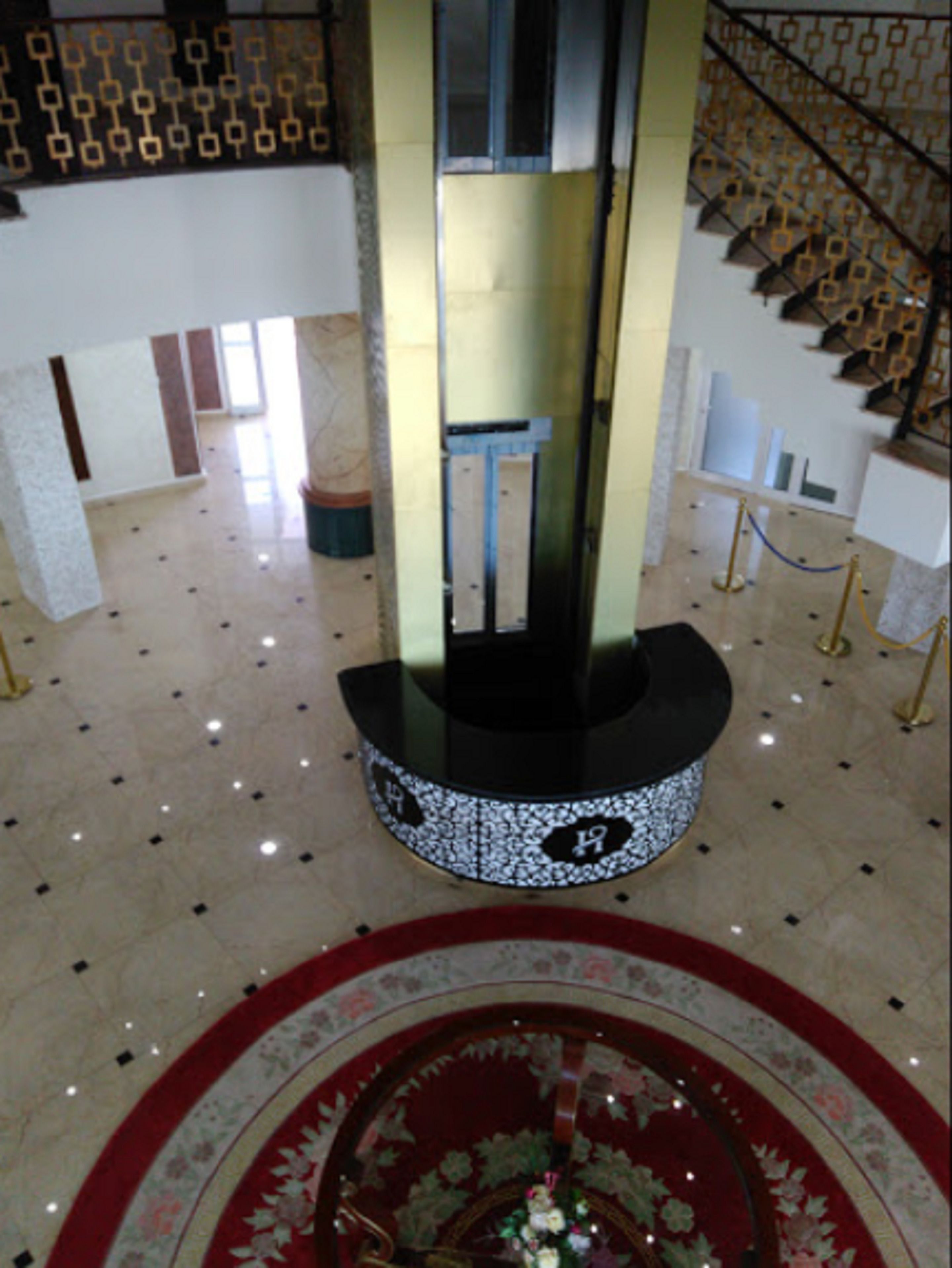 A grand staircase with a patterned railing, a central elevator, and a decorative circular floor design.