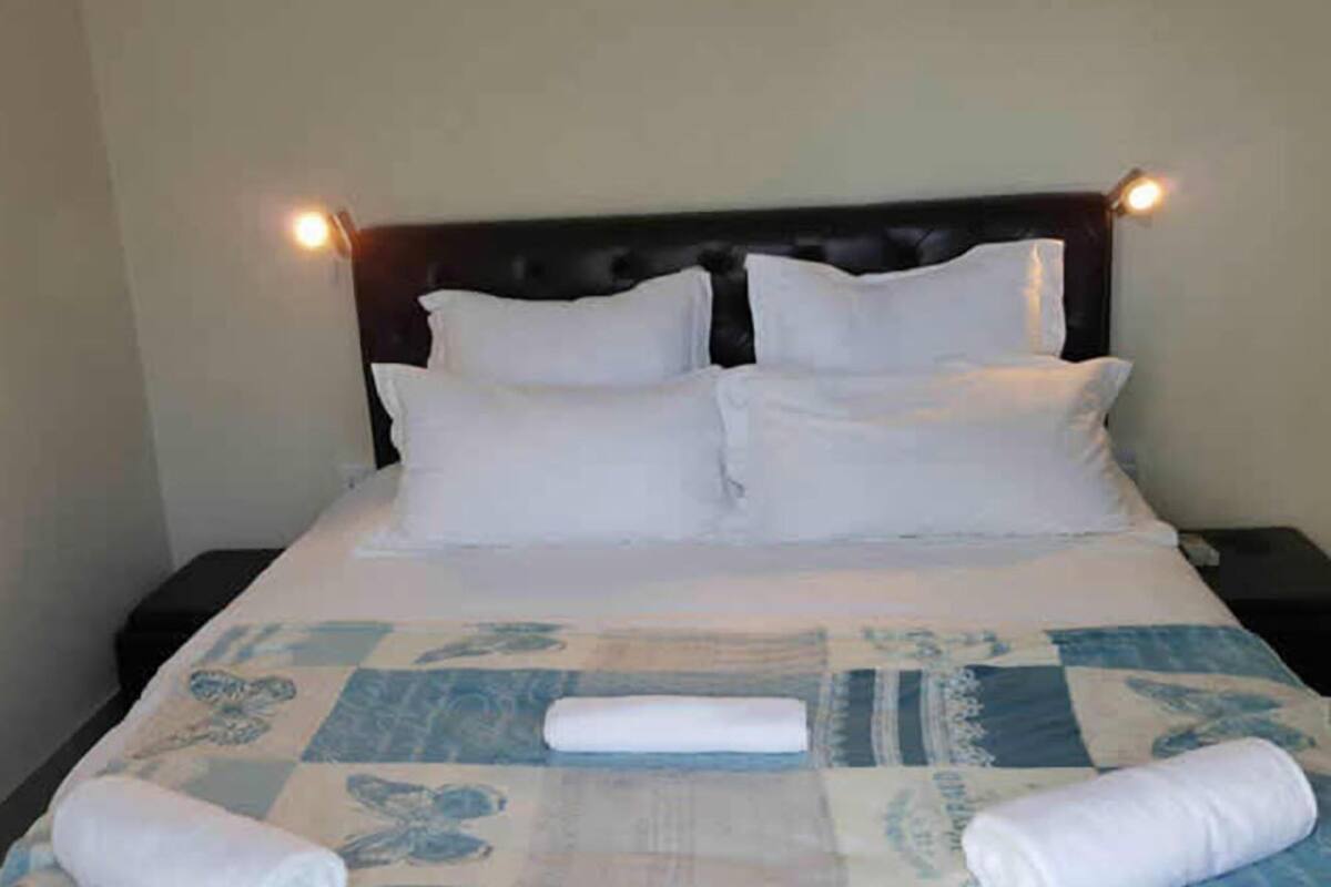 Una cama bien hecha con sábanas blancas y colcha, cabecera oscura y dos lámparas de noche.