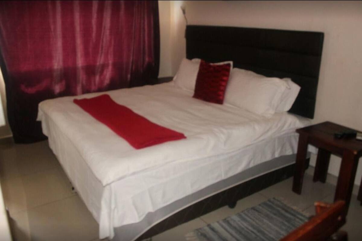 Una cama bien hecha con ropa blanca y una manta roja.
