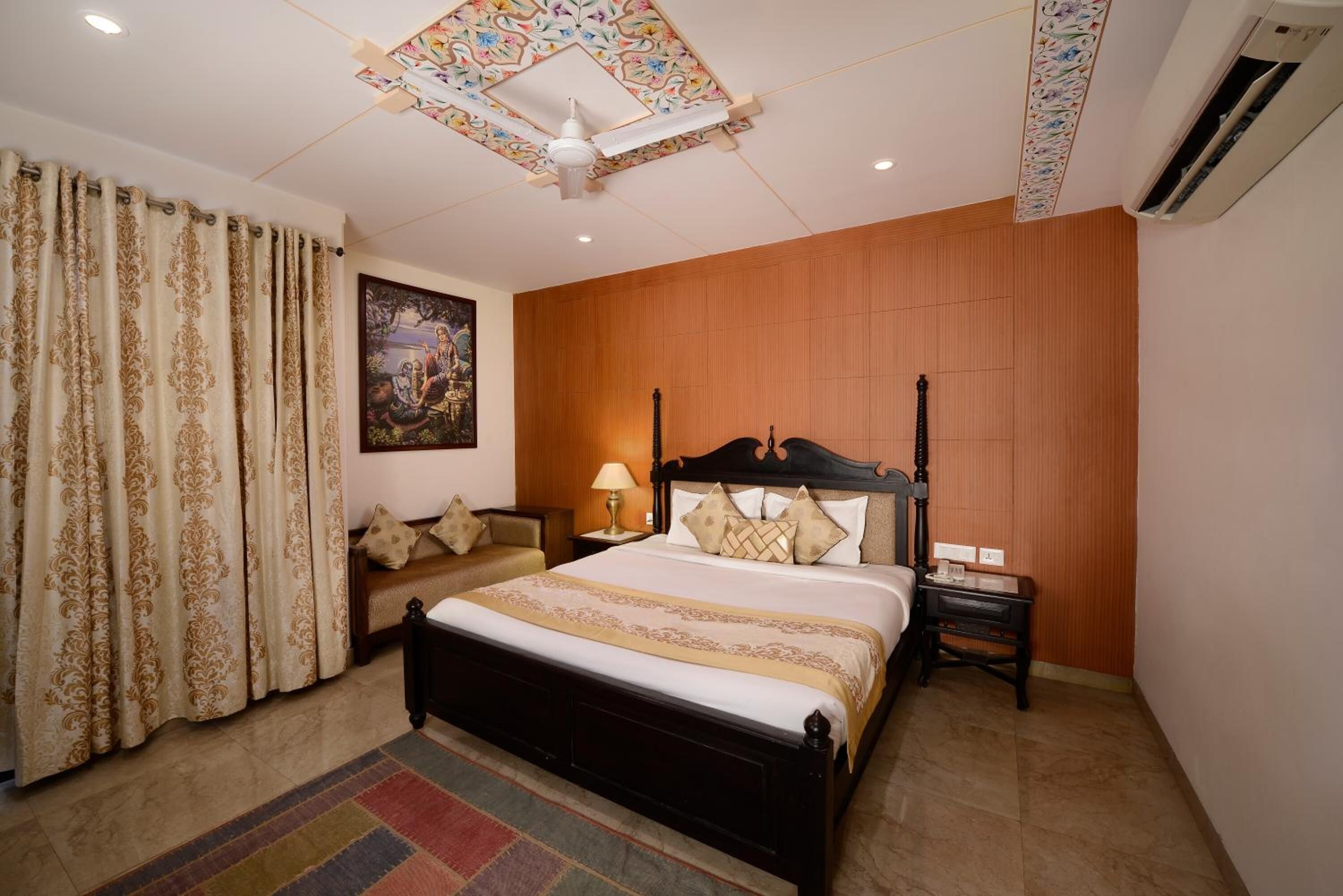 A bedroom with a bed, a nightstand, a lamp, a sofa, and a painting on the wall.