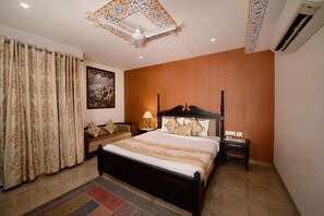 A bedroom with a bed, a nightstand, a lamp, a sofa, and a painting on the wall. - Radhey Ki Haveli (Danta Ramgarh)