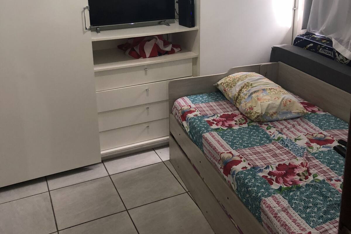 A bedroom with a bed, a TV, a wardrobe, and a window with curtains.