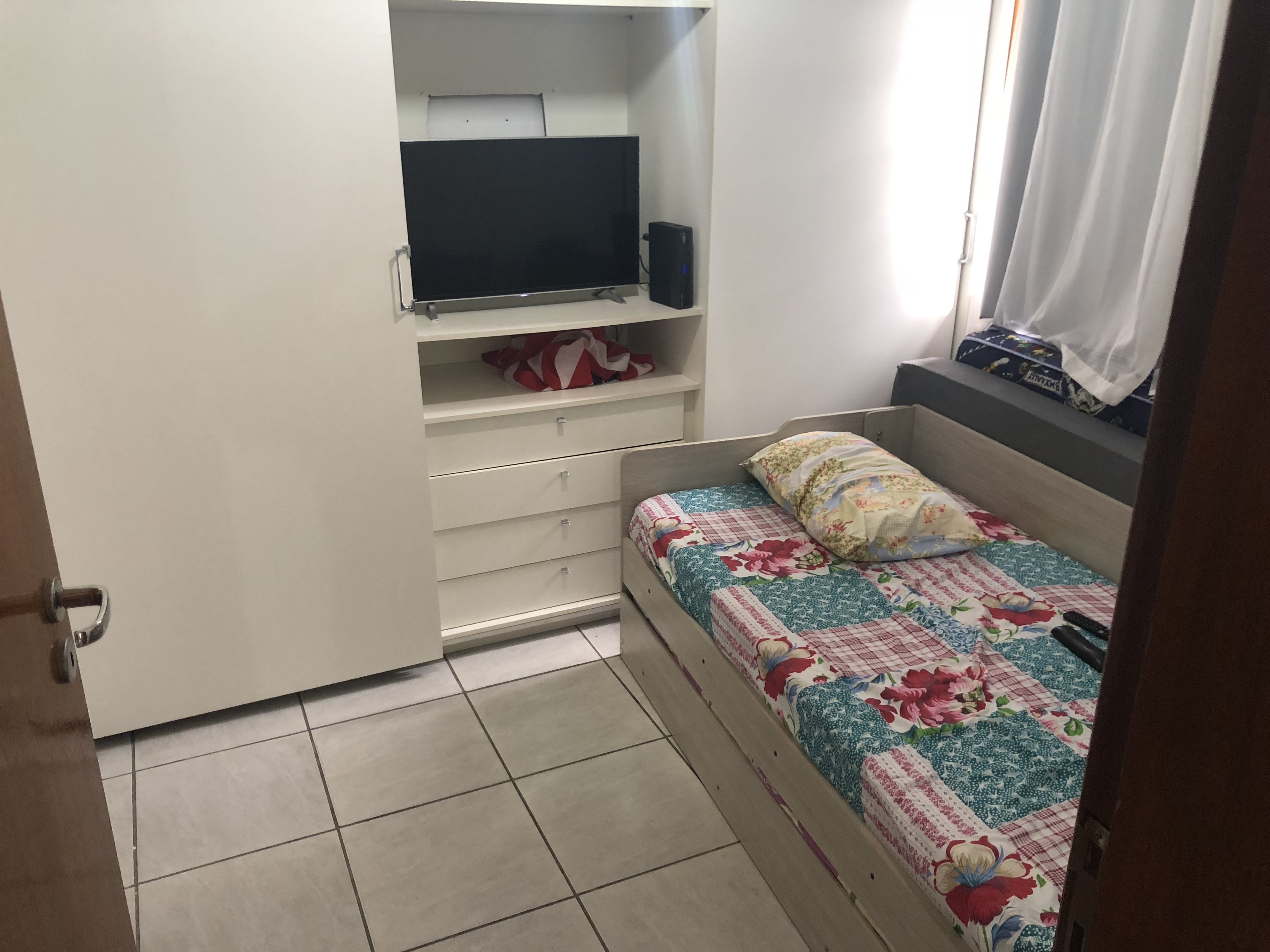 A bedroom with a bed, a TV on a shelf, and a wardrobe.