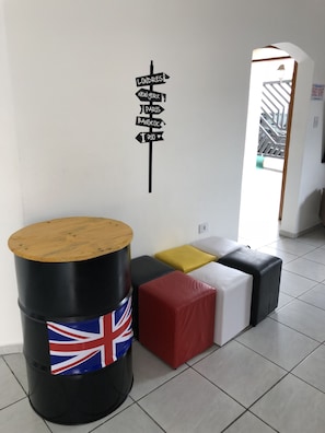 Una habitación con un cartel direccional en la pared, un barril de madera con la bandera del Reino Unido y un área de descanso con cojines.