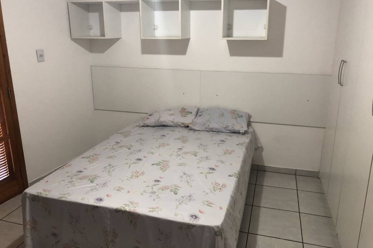 A small bedroom with a single bed, floral bedspread, and three wall-mounted shelves.