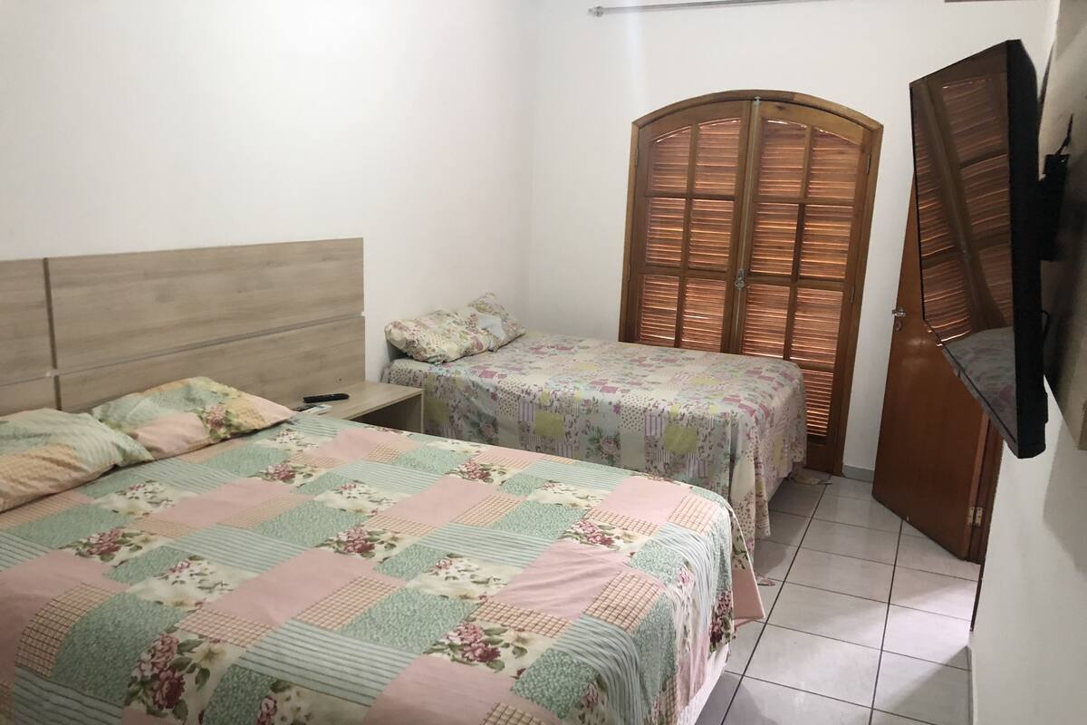 A room with two beds, a wooden headboard, a nightstand, a wooden wardrobe, and a television.