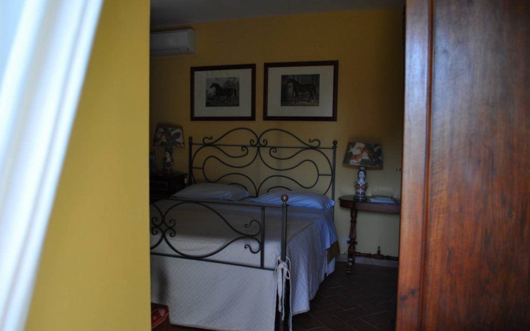 Een slaapkamer met een metalen bedframe, twee ingelijste foto’s aan de muur en een nachtkastje met een lamp.
