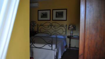 A bedroom with a metal bed frame, two framed pictures on the wall, and a bedside table with a lamp.