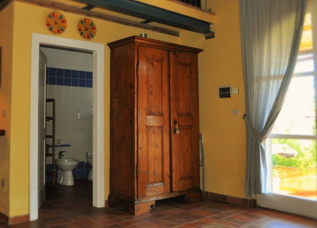 Ein Zimmer mit Holzschrank, Badezimmer mit blauen Fliesen und einem mit Vorhängen versehenen Fenster.