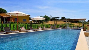 A swimming pool with lounge chairs and umbrellas, surrounded by a landscaped garden and a hillside.
