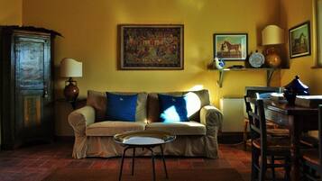 Una sala de estar con un sofá, una mesita redonda, un aparador y varias decoraciones en las paredes.