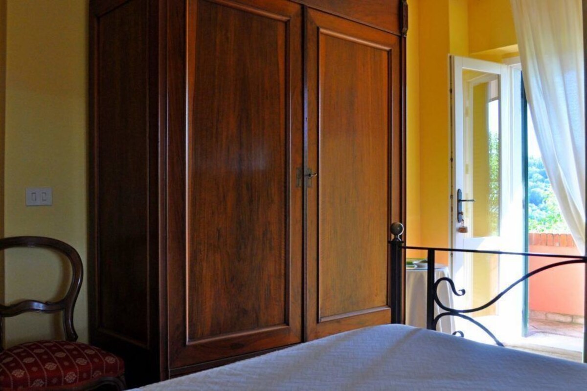 A bedroom with a bed, wooden wardrobe, chair, and a balcony with curtains.