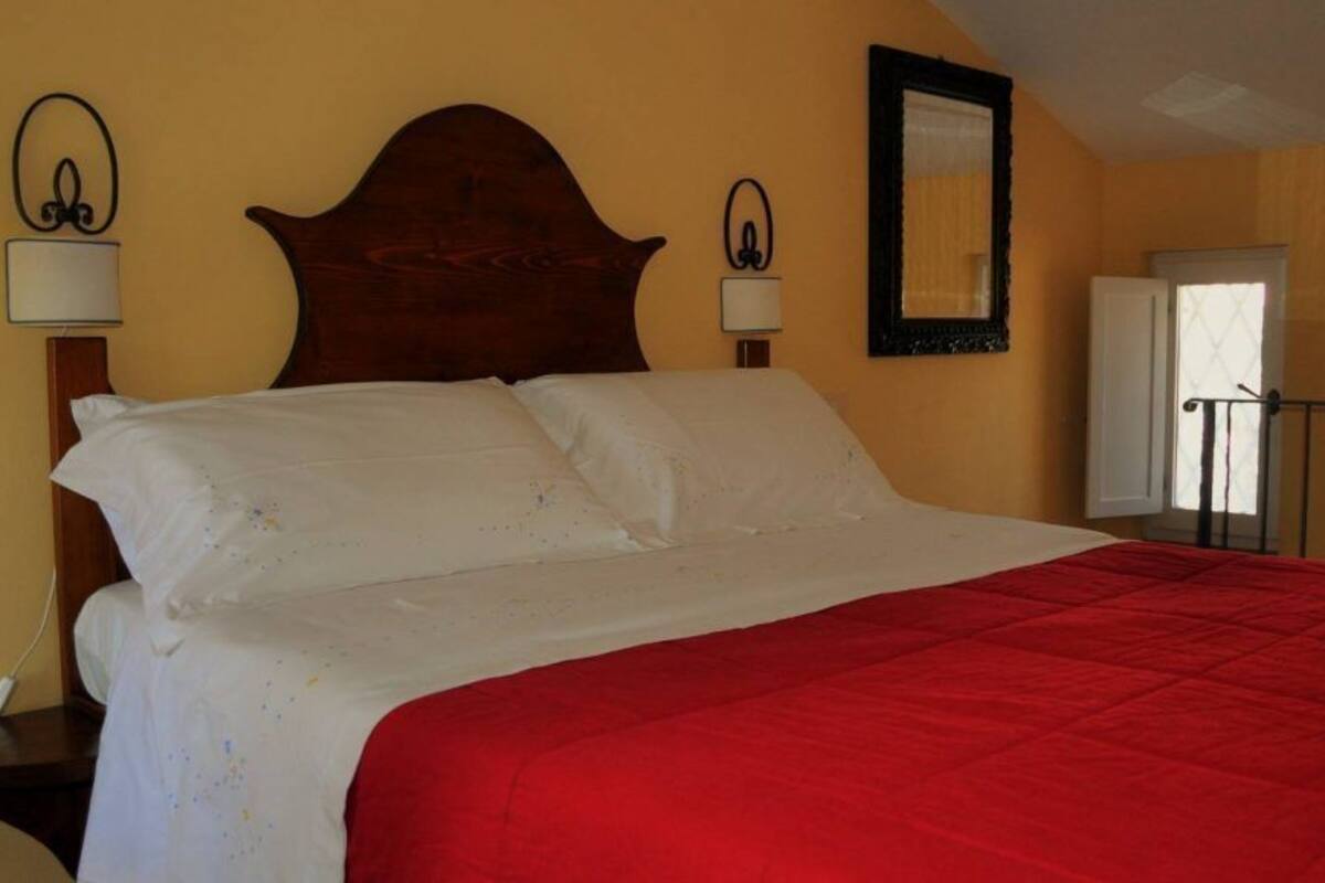 A bed with a red bedspread, two bedside lamps, a wooden headboard, and a mirror on the wall.