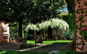 A garden with wicker furniture, a pergola with hanging vines, and a building with a tiled roof. - Podere L'Olmaia (Manciano)