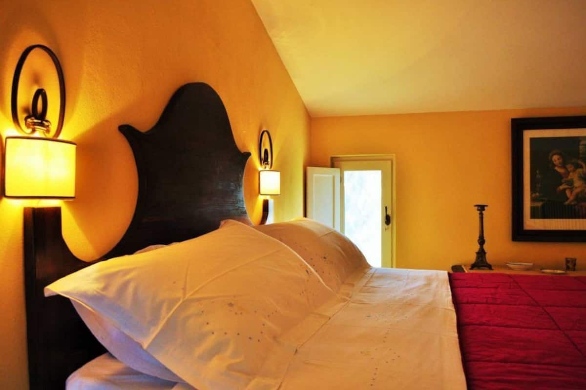 A hotel room with a large bed, two wall-mounted lamps, a framed picture, and a door.