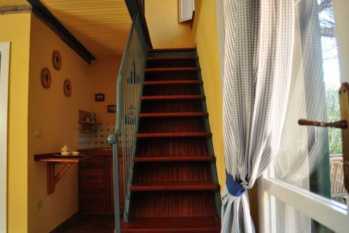 A staircase with wooden steps and a metal railing, leading to a room with a window covered by a checkered curtain.