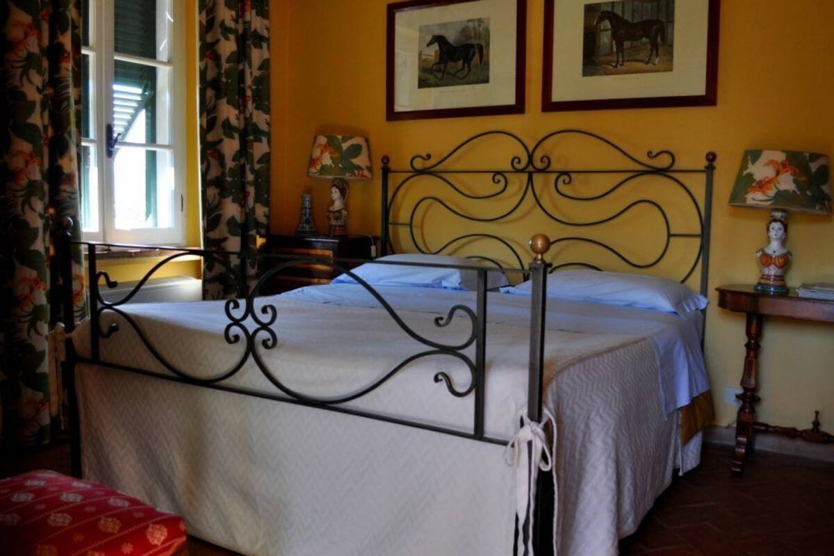 A bed with a metal frame, a bedside table with a lamp, and two framed pictures on the wall.