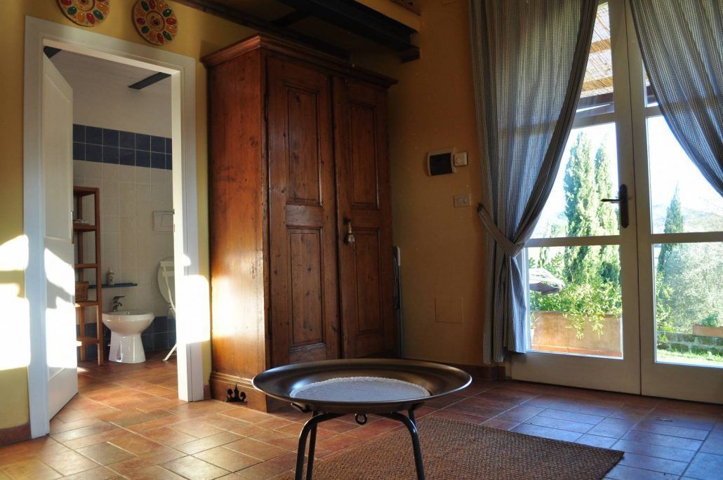 A room with a wooden wardrobe, a bathroom with a white sink and blue tiles, and a large window with curtains.