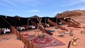 A desert tented area with tables set for dining, a hanging chair, and traditional decor. - Mazayen Rum Camp (Wadi Rum)