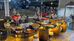 A buffet with various dishes and drinks, arranged on tables with a view of the cityscape outside. - Mazayen Rum Camp (Wadi Rum)