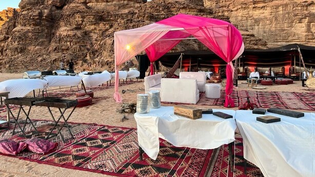 An outdoor event setup with tents and tables on a sandy area with rocky cliffs in the background. - Mazayen Rum Camp (Wadi Rum)