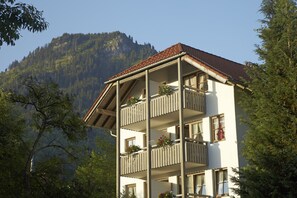 A multi-story building with balconies, surrounded by trees and mountains.