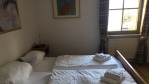 Camera d'albergo con due letti, lenzuola bianche, un quadro appeso al muro, una finestra con tende e un termosifone.
