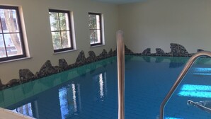 Una piscina interna con acqua cristallina, pareti in pietra e finestre.