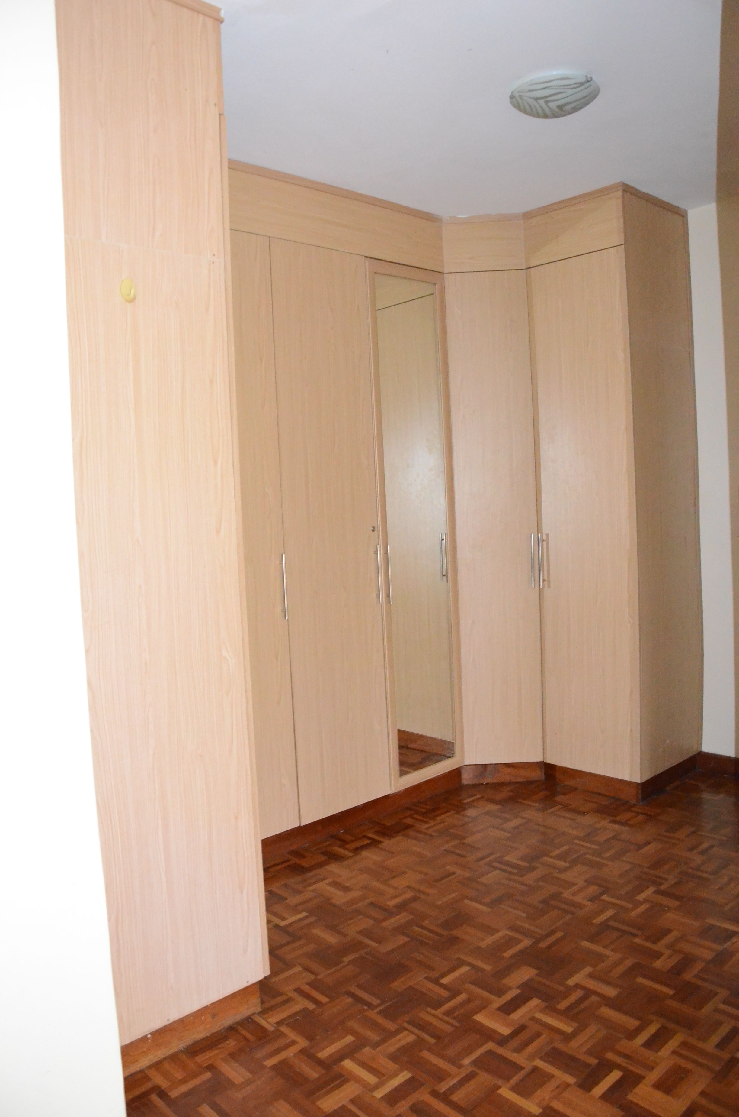 A room with a wooden floor and a large wardrobe with multiple doors.