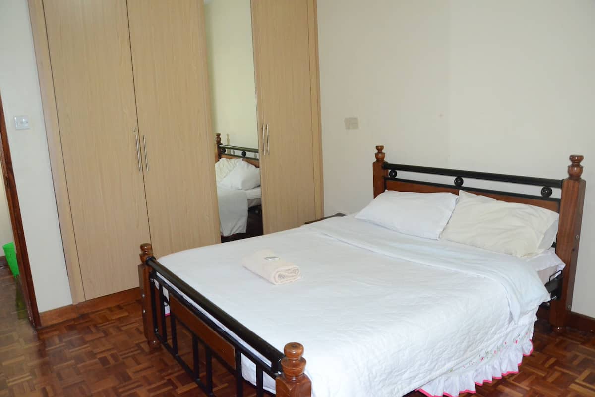 A neatly made bed with white linens and a folded towel, wooden wardrobe with mirrored doors, and a wooden floor.