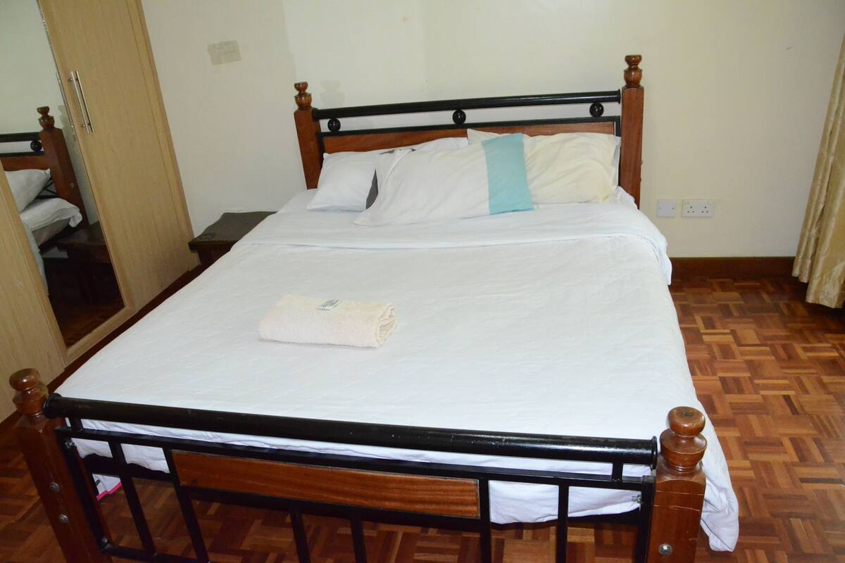 A neatly made bed with white linens and a folded towel, a wooden headboard, and a wooden floor.