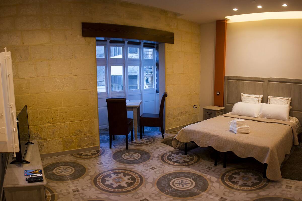 A hotel room with a bed, a desk, a chair, and a window.