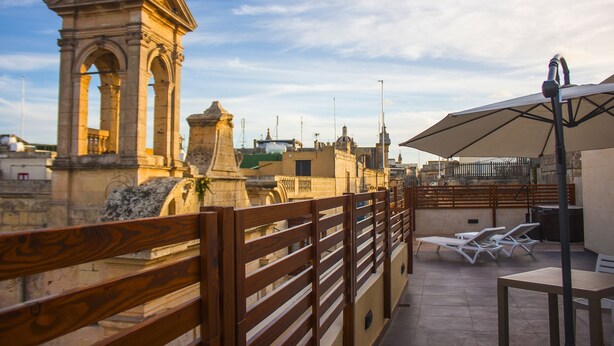 A rooftop terrace with a wooden railing, white lounge chairs, and a large umbrella. - Casa Azzopardi Suites (Rabat)