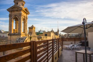 Terraza en la azotea con barandilla de madera, sillas de lounge blancas y un paraguas grande.