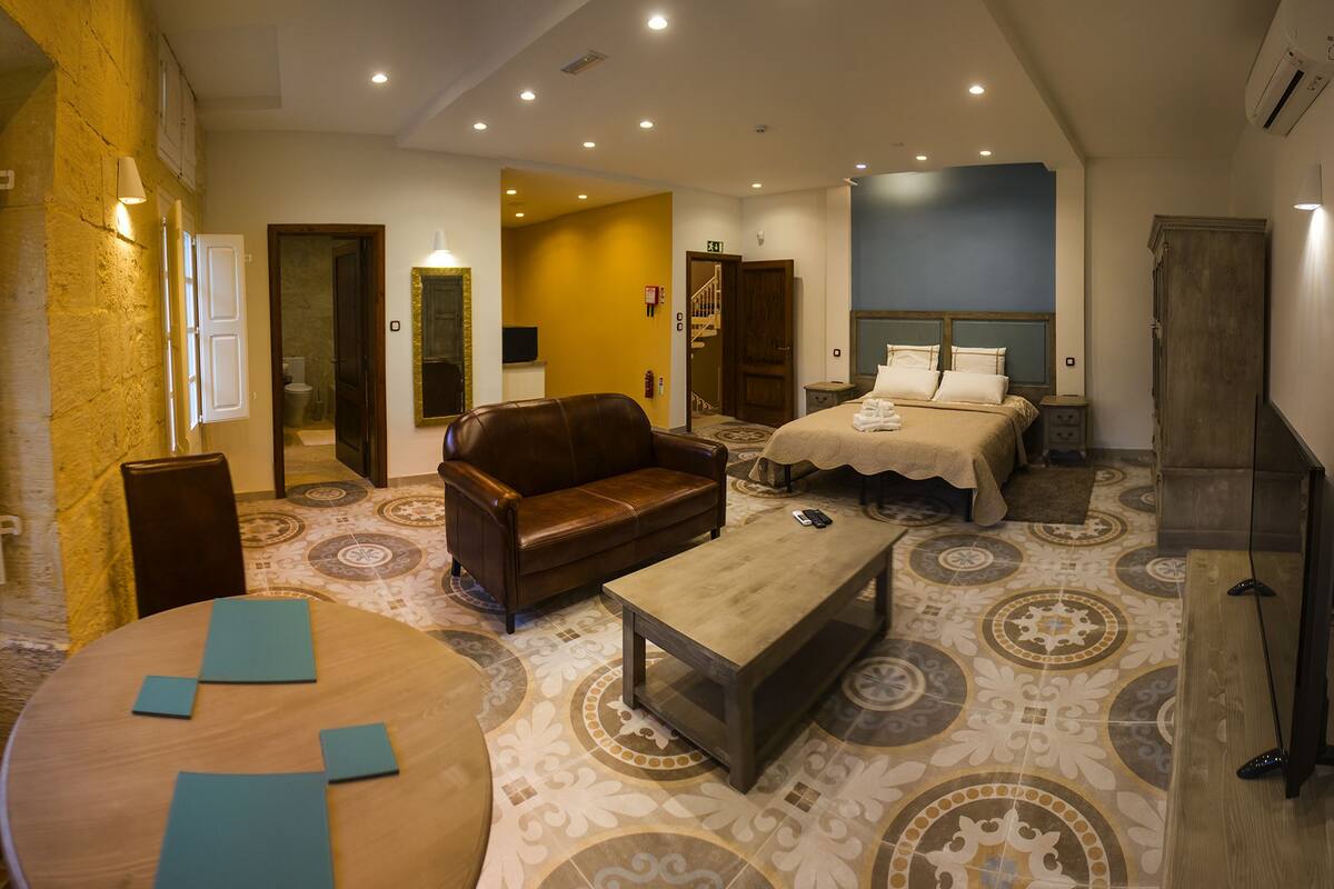 A spacious hotel room with a large bed, a leather sofa, a round table, and a TV.