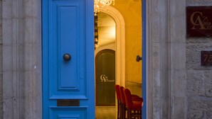 A blue door with a decorative metal frame, leading to a room with a chandelier and red chairs. - Casa Azzopardi Suites (Rabat)