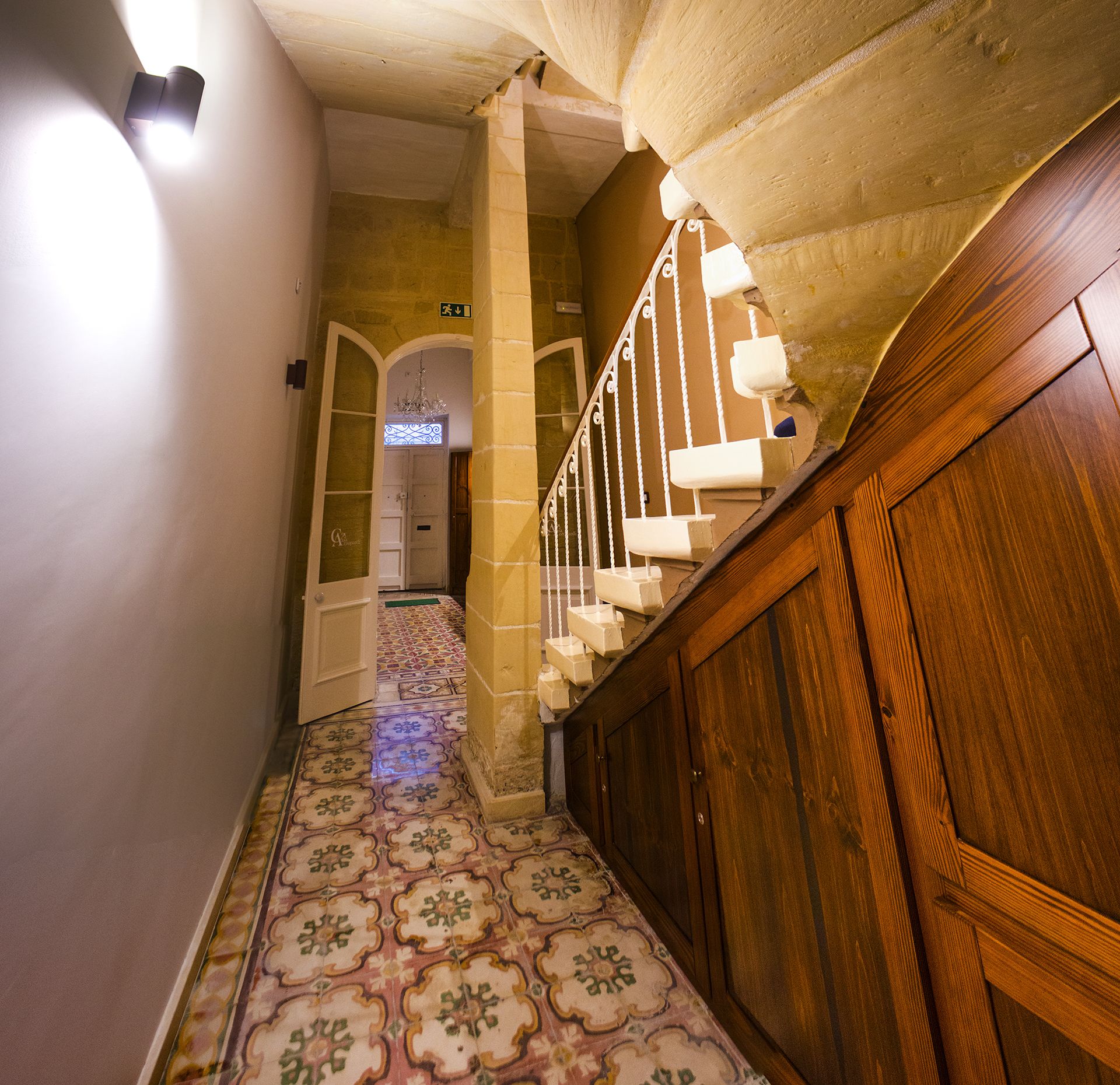 Un couloir avec un sol à motifs, un escalier en bois et une porte au fond.