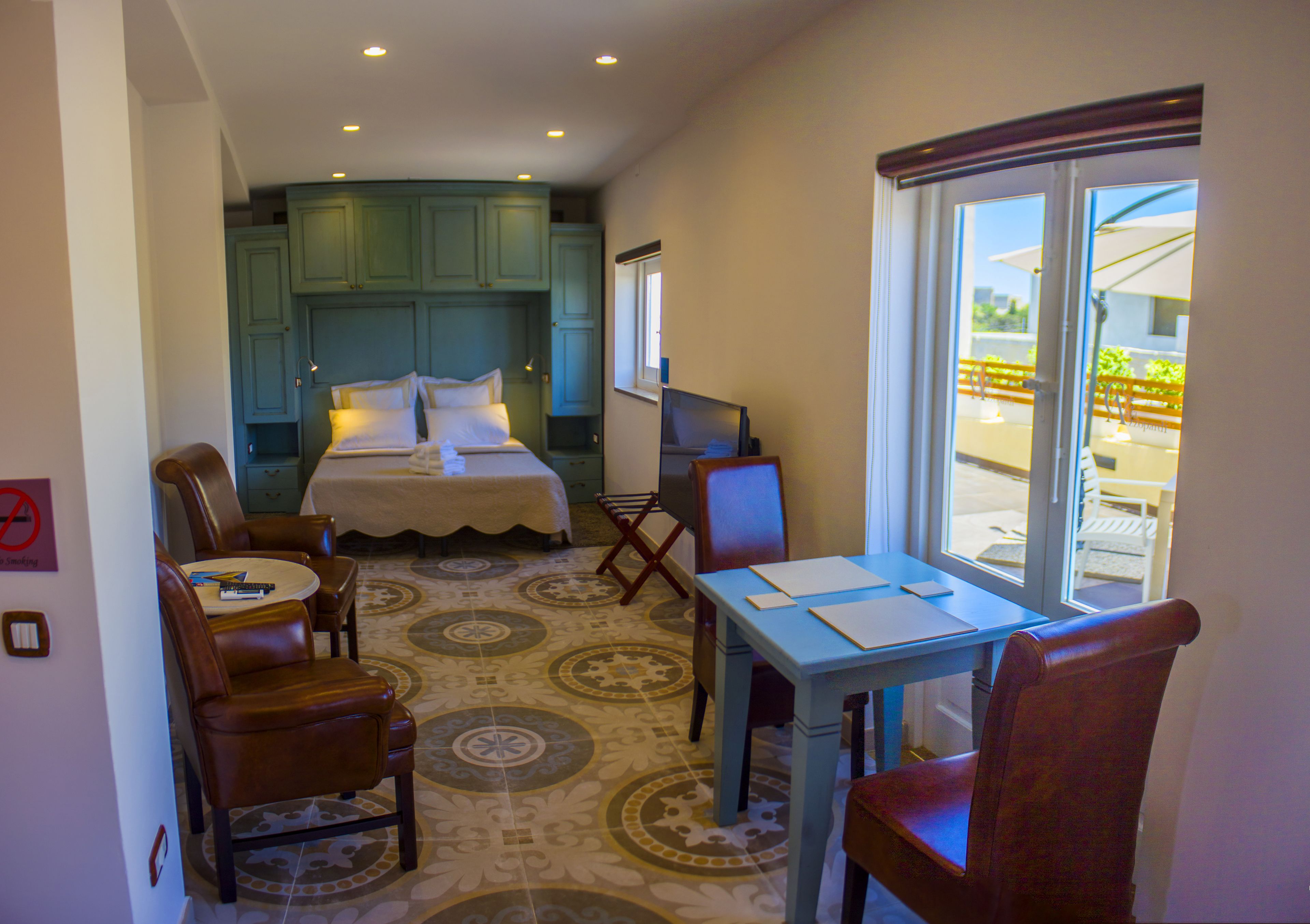 A bedroom with a bed, a desk, and a chair. There is a window with a view of the outside.