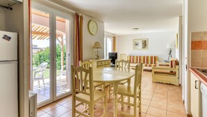A dining area with a table and chairs, a sofa, a TV, and a kitchen area with a refrigerator and stove. - Vacancéole - Port Minervois (Homps)