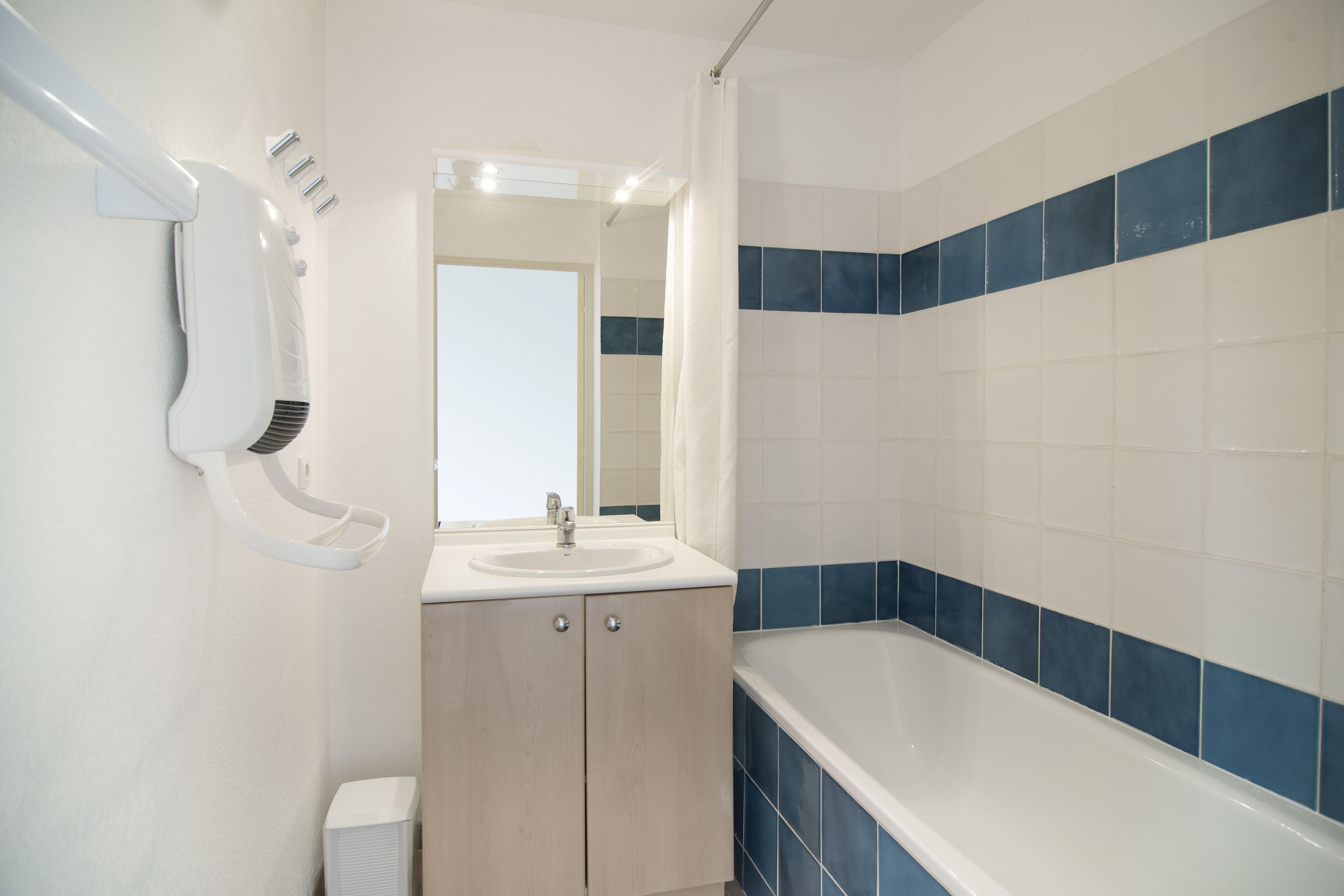 Une salle de bain avec un lavabo, un miroir et une baignoire dont les carreaux sont bleus.